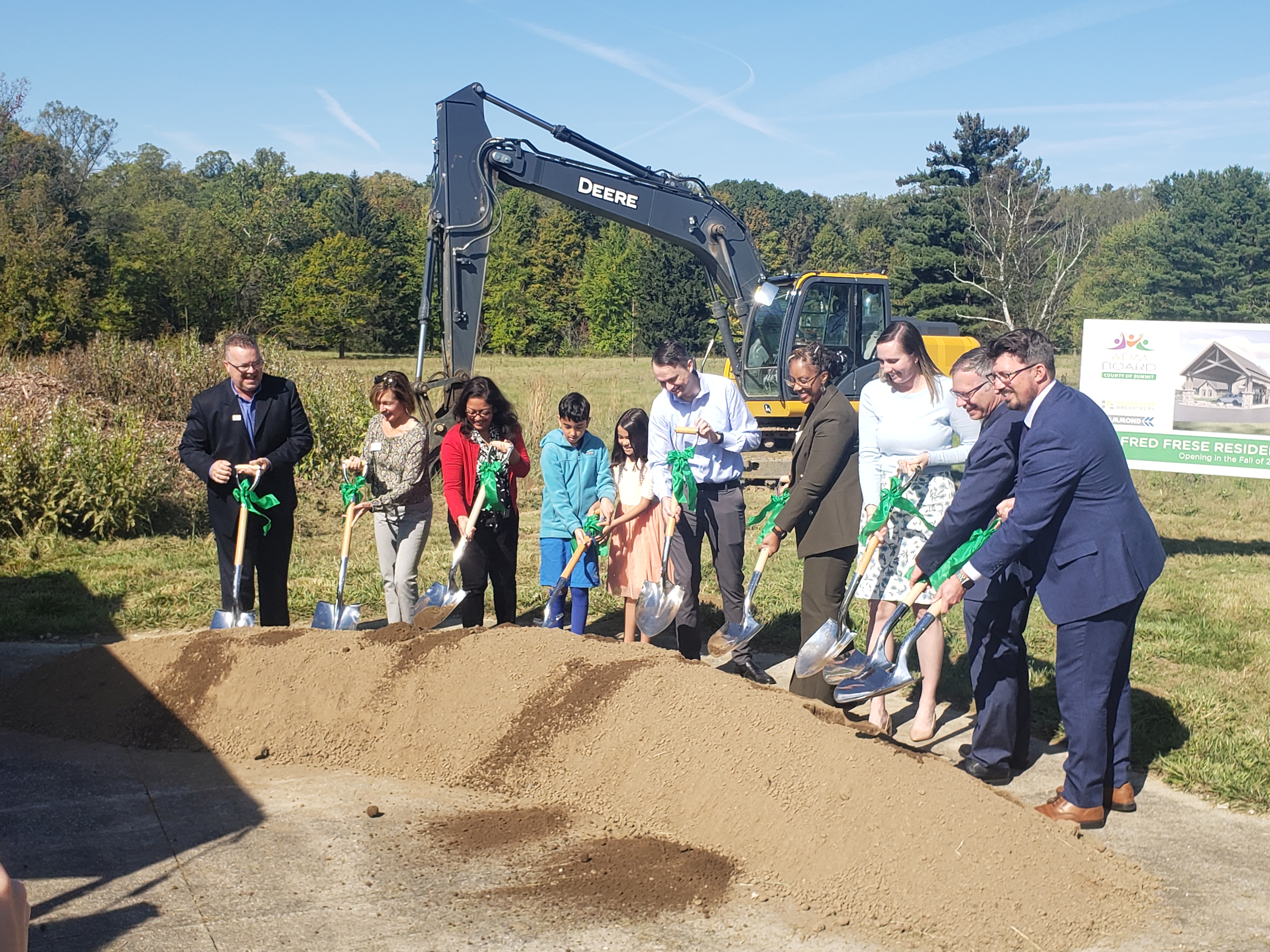 A row of people stand behind a dirt mound while tossing shovelfuls of dirt in front of them.