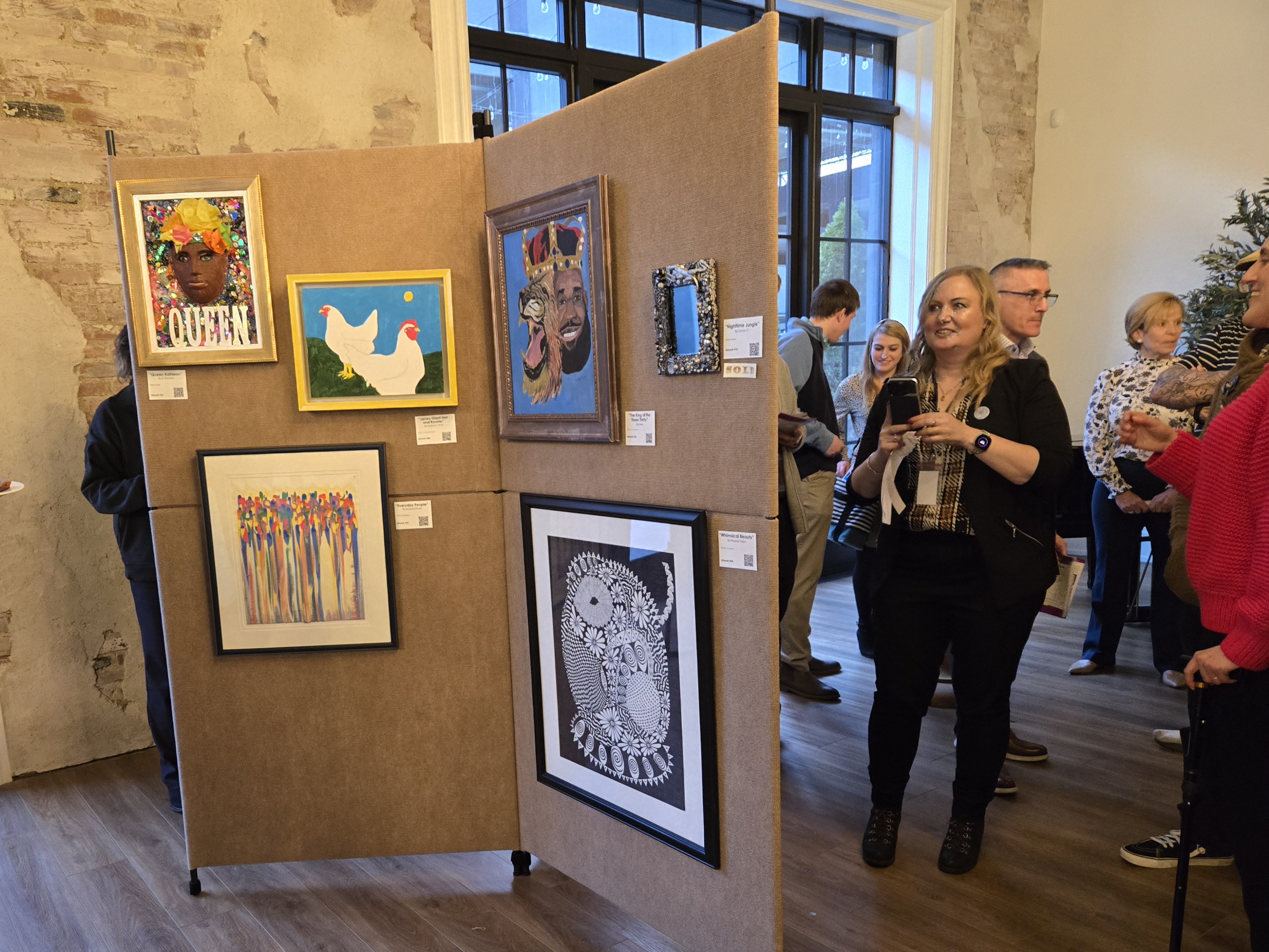 A woman dressed in black looks at art displayed on beige walls at Art of Recovery.