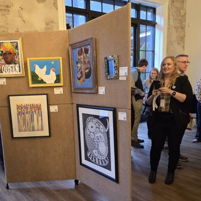 A woman dressed in black looks at art displayed on beige walls at Art of Recovery.