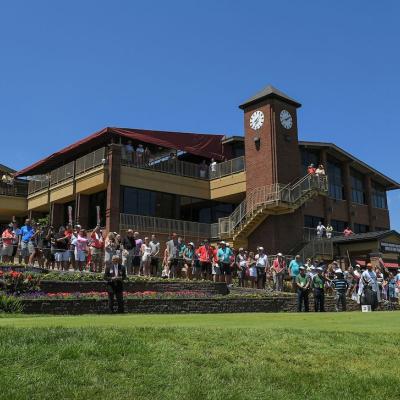 A photo of Firestone Country Club with a crowd in front, a green lawn in the foreground and a blue sky in the background