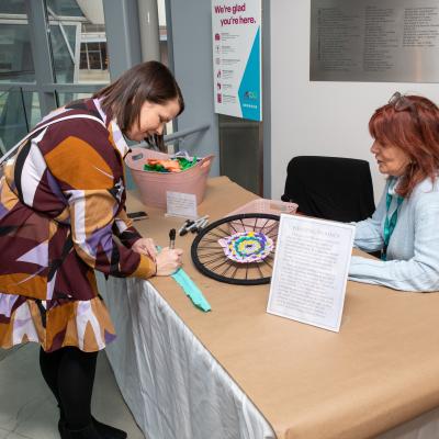 A woman in a dress looks over an art project attended by another woman.