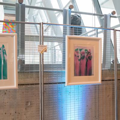 Three pastel works of art in white frames hanging on a metal screen.