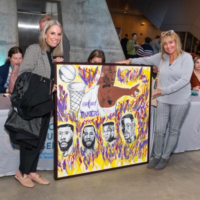Two women show off a large work of art purchased at Art of Recovery.