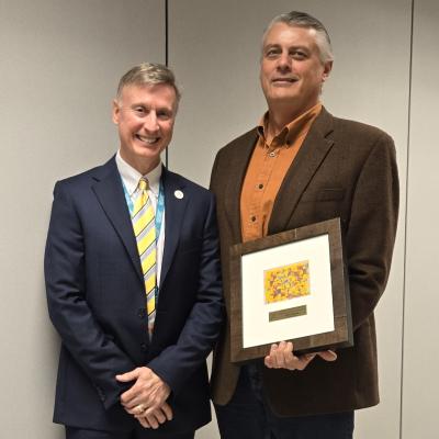 CSS CEO Bob Stokes stands with Marty Ganzer, who is holding a framed piece of art.
