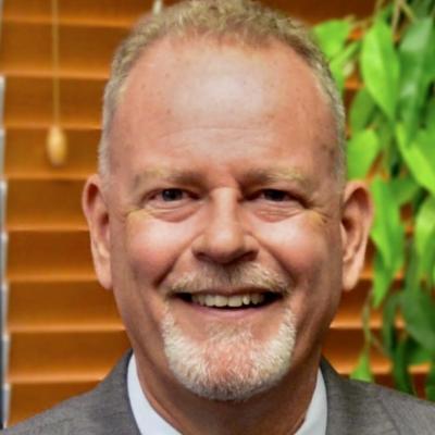 Head and shoulders photo of Michael Bullock wearing a white shirt and gray jacket in front of a brick wall