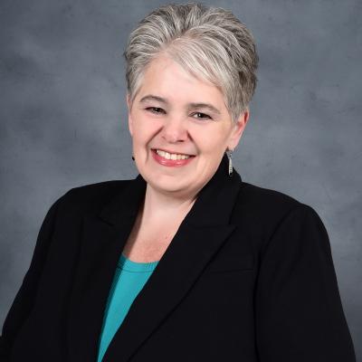 A professional head and shoulders shot of Kim Meals in a black blazer and teal top.