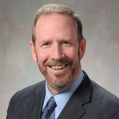 Photo of Michael Gaffney in a gray suit jacket, blue shirt and tie.