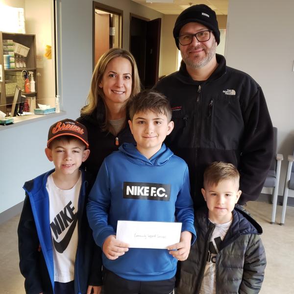 12-year-old Isaac Waldeck holds a donation check to CSS while surrounded by his mother, father and two younger brothers.